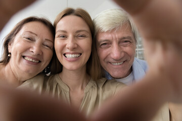 Happy senior parents and adult child woman portrait shot in hand heart shaped frame. Cheerful elder...