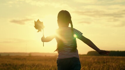 Cute little girl running with windmill pinwheel rotate toy at summer field sunset sunrise sky back view slowmo. Female kid child spinning wind turning plaything freedom childhood countryside meadow - obrazy, fototapety, plakaty