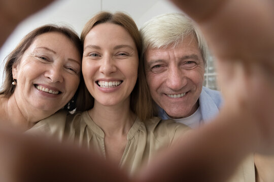 Happy senior parents and adult child woman portrait shot in hand heart shaped frame. Cheerful elder mom, dad, daughter having fun, posing together, looking at camera, laughing, smiling