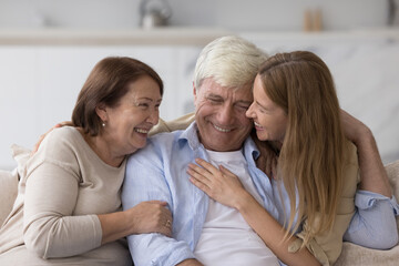 Cheerful adult woman hugging older senior parents, smiling, laughing, chatting with mom and dad, having fun, enjoying relationship, affection, care. Family celebrating fathers day