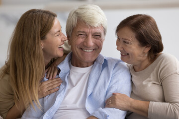 Happy mature wife and adult daughter woman hugging senior grey haired dad, congratulating on...