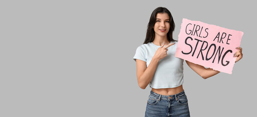 Young woman holding poster with text GIRLS ARE STRONG on grey background with space for text. Feminism concept