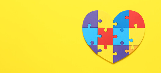 Heart made of colorful puzzle pieces on yellow background. Concept of autism spectrum disorder