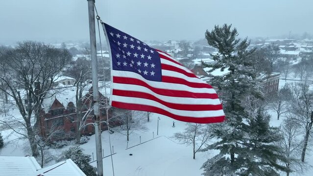 Aerial establishing shot of an American flag waving over Gettysburg College. Snowy winter scene at university campus in the USA.