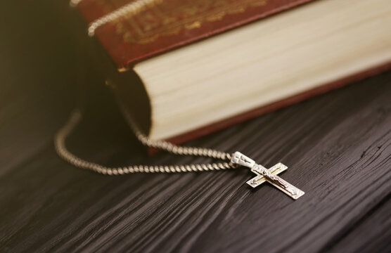 Silver necklace with crucifix cross on christian holy bible book on black wooden table. Asking blessings from God with the power of holiness, which brings luck and shows forgiveness.