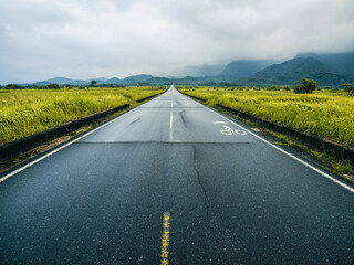 Straight road leading to the mountains, under cloudy skies.	