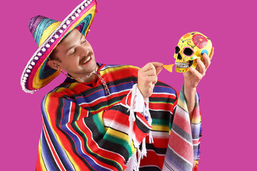 Handsome young Mexican man with painted skull and nachos on magenta background. Celebration of Day...