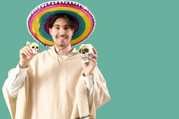 Handsome young Mexican man with painted skulls on green background. Celebration of Day of the Dead