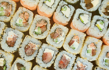 Close-up of a lot of sushi rolls with different fillings lie on a wooden surface. Macro shot of cooked classic Japanese food with a copy space.