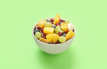 Bowl with fresh fruit salad on green background