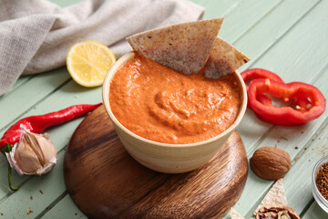 Bowl of tasty muhammara on green wooden background