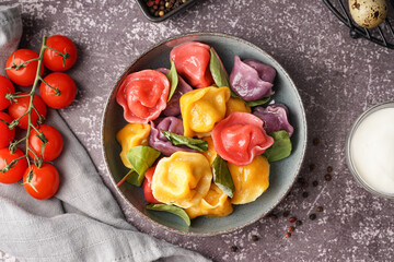 Bowl of boiled colorful dumplings with spinach and tomatoes on dark table