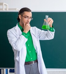 Young male chemist teacher in front of blackboard