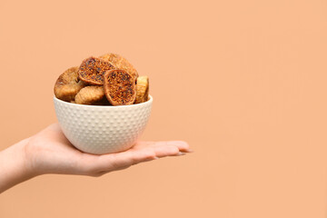 Female hand holding bowl with tasty dried figs on beige background