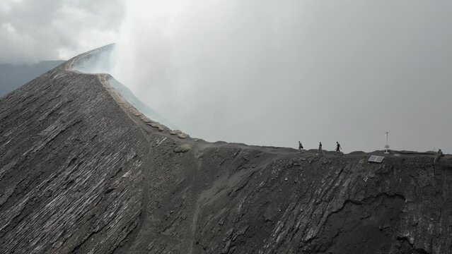 Steam billows as tourists walk on narrow volcano rim trail at Mt Bromo