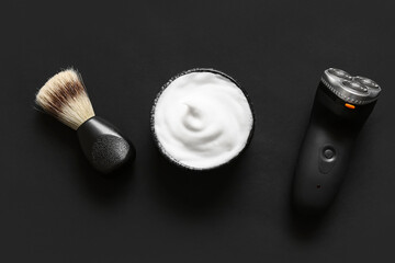 Bowl of shaving foam with brush and electric shaver on black background