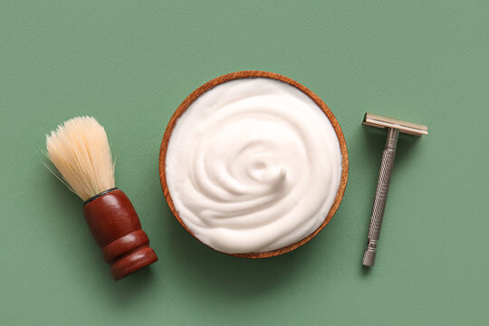 Bowl of shaving foam with brush and razor on green background
