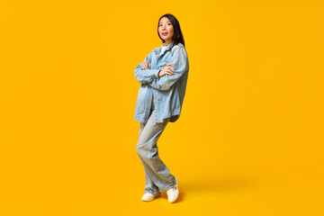 Fototapeta na wymiar Beautiful young thoughtful Asian woman in stylish denim clothes on yellow background