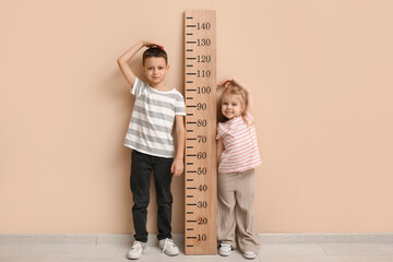 Cute little children measuring height near beige wall