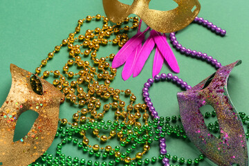 Colorful beads with carnival masks and feathers for Mardi Gras celebration on green background