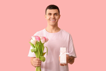 Handsome man with gift box and tulips on pink background
