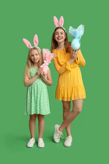 Cute little girl and her mother in bunny ears with Easter gift eggs on green background