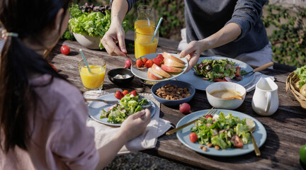 Mother and daughter eating fresh vegetable salad with fresh vegetables, tomatoes, bell pepper, potato, fruits and dipping sauces on wooden desk at outdoor garden, Conceptual of party family healthy