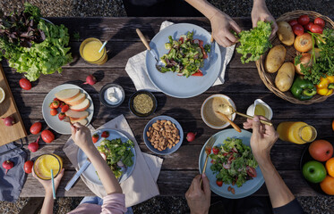 Father mother and daughter eating fresh vegetable salad with fresh vegetables, tomatoes, bell pepper, potato, fruits and dipping sauces on desk at outdoor garden, Conceptual of party healthy
