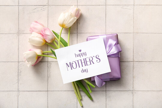 Card with text HAPPY MOTHER'S DAY, gift box and tulip flowers on light tile background