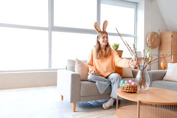 Young woman in bunny ears with willow branches and Easter eggs at home