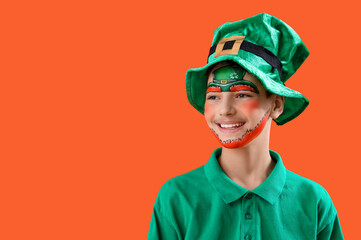 Funny boy with face painting and leprechaun's hat on orange background. St. Patrick's Day celebration