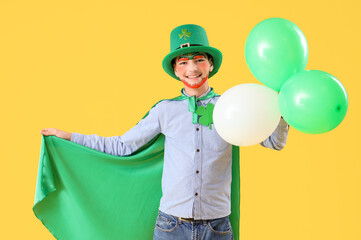 Funny boy with face painting, cape, leprechaun's hat and balloons on yellow background. St. Patrick's Day celebration