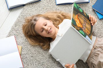 Naklejka premium Little girl reading book on floor at home