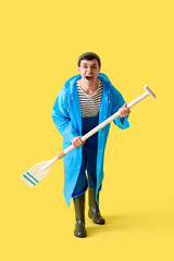 Young sailor in raincoat with paddle on yellow background