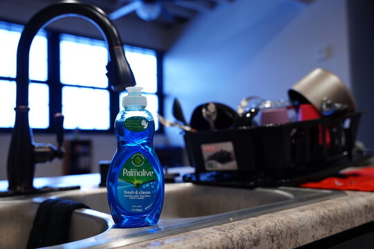A small bottle of Palmolive dish soap sits in front of a drying rack of dishes in the kitchen.