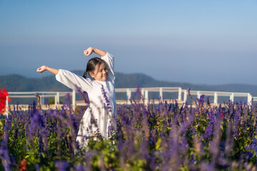Asian child or kid girl relax on beauty of many fresh flowers to happy smile on blue violet in nature flower field garden on holiday travel and mountain white bridge sky view at Yingyong flower garden