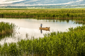 Fisherman is standing in the old, wooden rowboat and catching the fish on cloudy day. Karamik Lake...