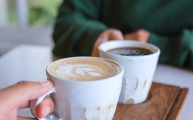 Closeup image of a couple people holding and clinking coffee cups together in cafe