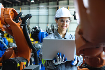 Caucasian female robotic engineer wearing helmet and safety glasses holding laptop smiles...