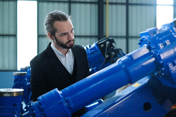 Bearded male engineer checking part number of automatic welding robotic arm in industrial robot...