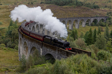 Naklejka premium Jacobite Great Western Railways Steam train crosses the Glenfinnan viaduct in the Scottish Highlands. Famous landmark in Scotland featured in Harry Potter