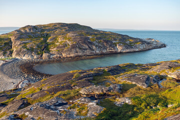 A serene summer evening by the turquise sea.  The rocky shores of Varangerfjord in beautiful and warm summer evening light, Finnmark, Norway.