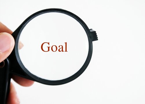 Hand holding magnifying glass focus on the text written GOAL. Concept of focusing on what matter most, goal in life.