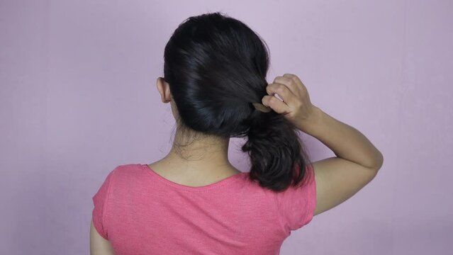 Young Asian woman unties her hair with an elastic hair band. Back view of young woman untying her hair from a ponytail.
