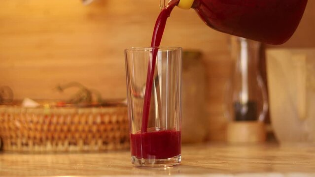 pouring a red smoothie from a glass jug into a glass at home. The juice is a mix of Strawberries, Raspberries, red currant, black currant, blueberries, blackberries, and water