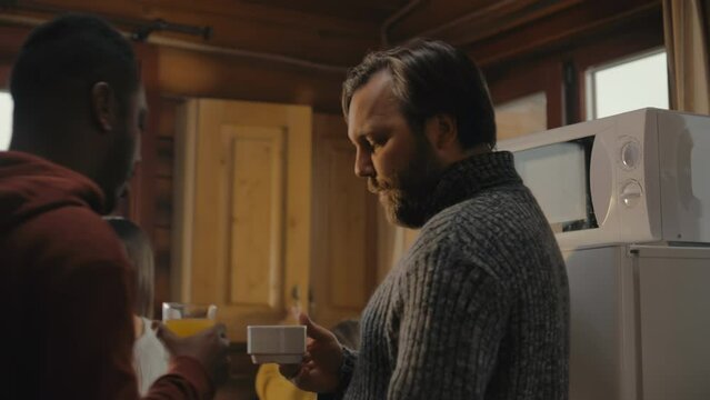 Multiethnic tourist friends drink coffee together in holiday house kitchen. Big travelers family stopped to rest in wooden cottage during vacation trip. Tourism and active leisure concept. Close up.