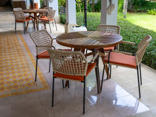 Two sets of coffee table with circular small table and four simple armchairs at a patio near a green garden.