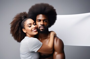 An African-American couple, a man with a naked torso and a woman who hugs and smiles at him, stand in the center of the frame, studio background gray blurred background, banner with space for text