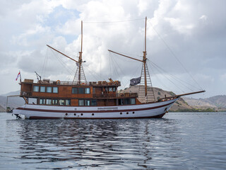 A classic Indonesian Pinisi boat in stationary state on calm water under bright white clouds.
