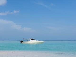 A small white speedboat anchored in the middle of turquoise water near a white sand beach.